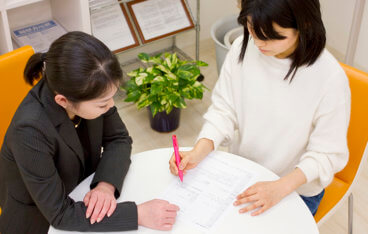スーツを着た女性が求職者の女性に書類に関して指導をしている写真